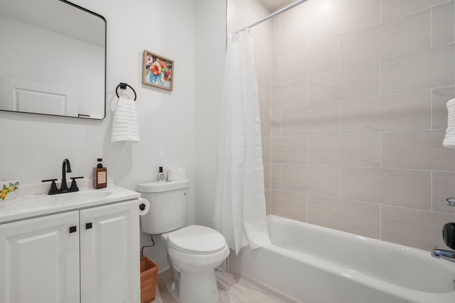 Full bathroom with white vanity, black fixtures and tiled tub surround