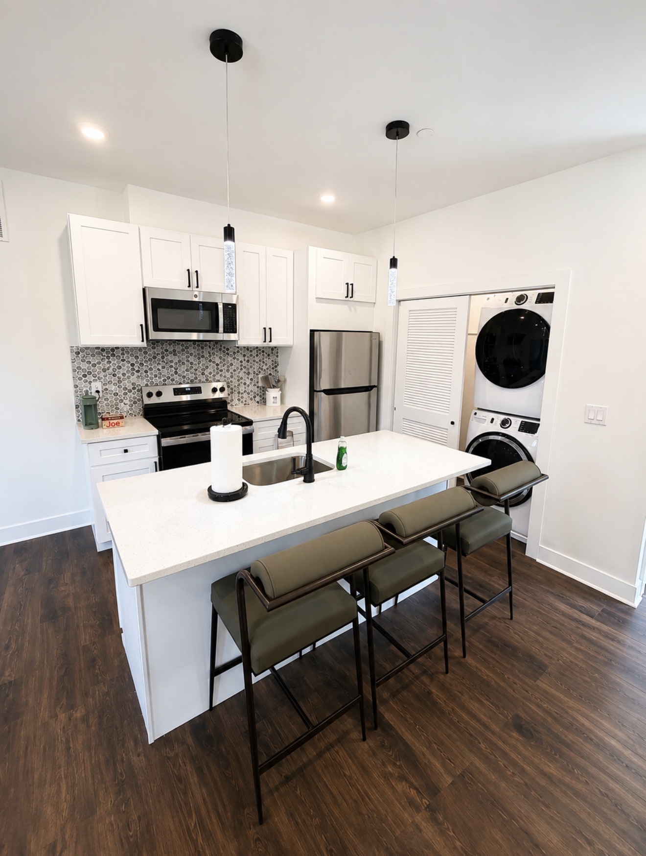 Kitchen with white shaker cabinets, island sink, hex tile backsplash and a louvered laundry closet