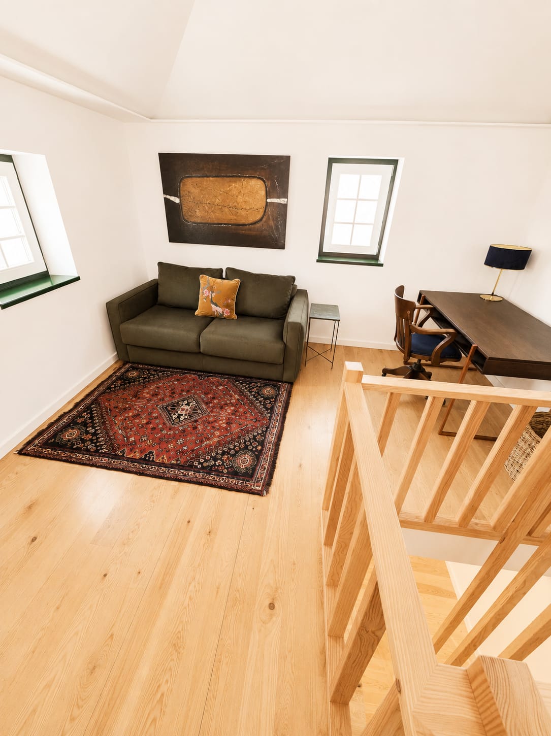 Upper-level lounge with olive loveseat, Persian rug and a dark wood writing desk