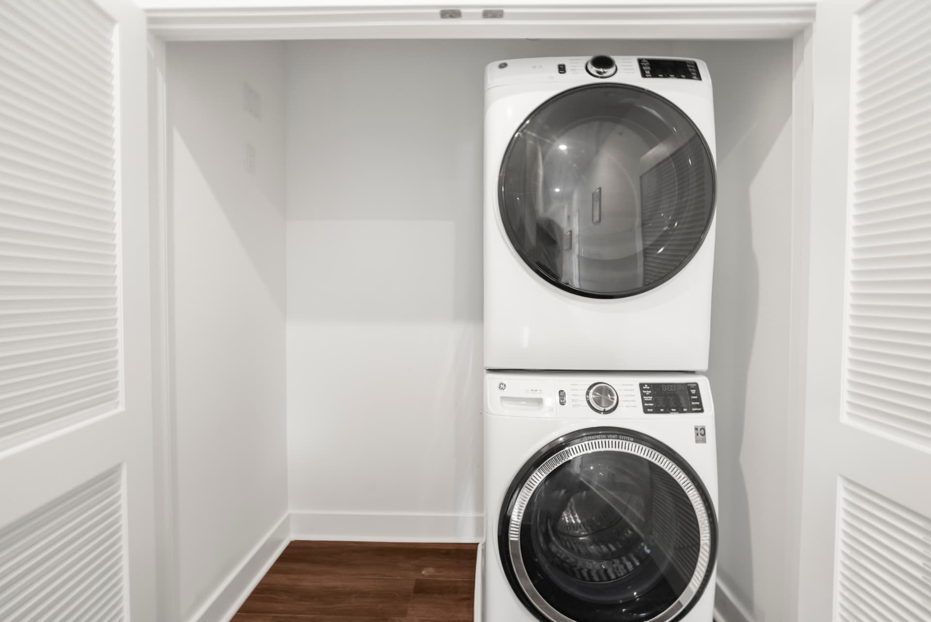 Stacked GE washer and dryer inside a louvered in-unit laundry closet