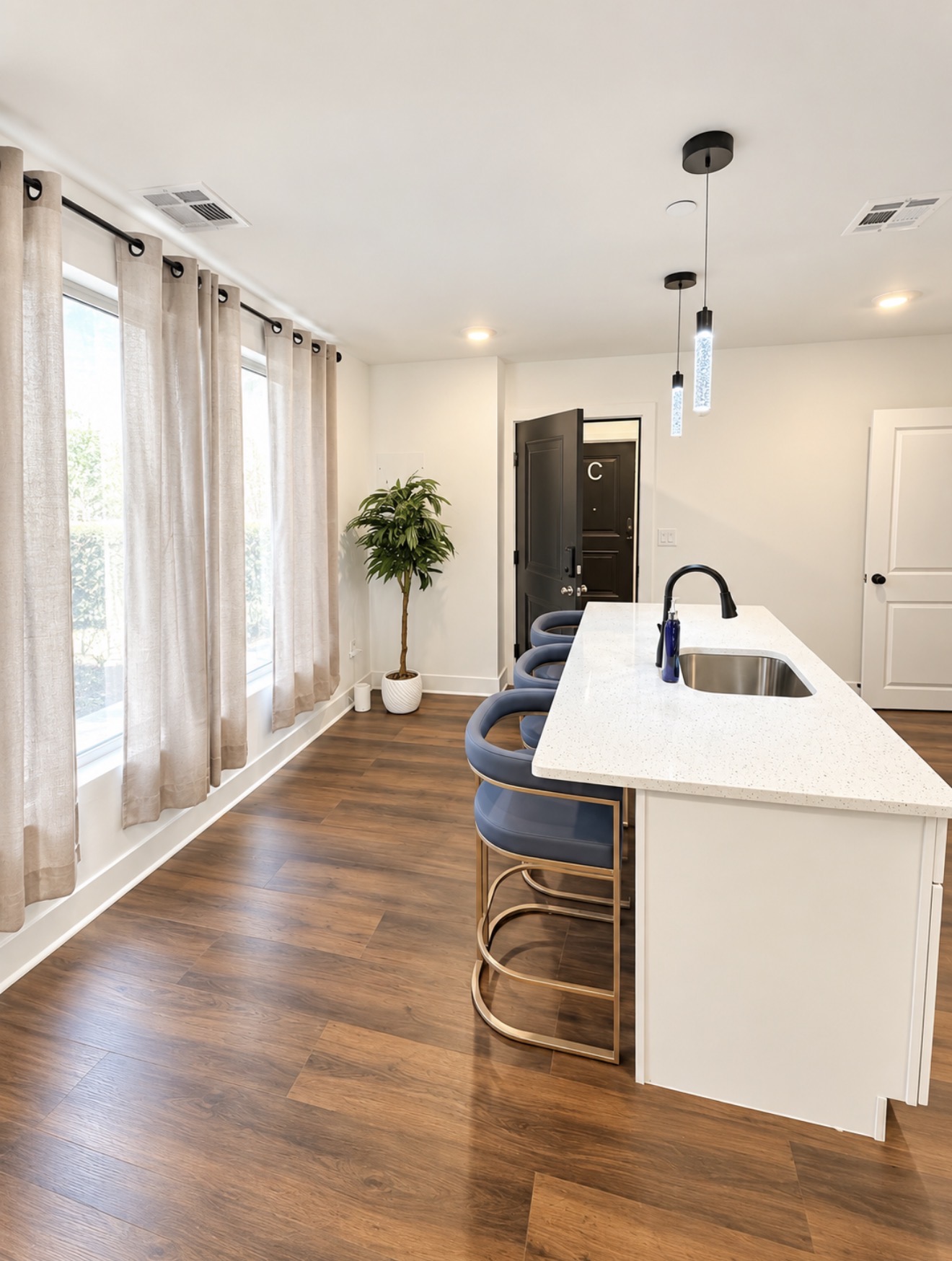 Kitchen island with bar stools and large windows looking toward the entry