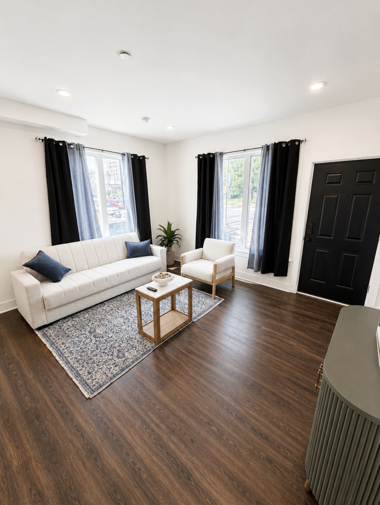 Living room with cream sofa and armchair beside two large windows dressed in black curtains