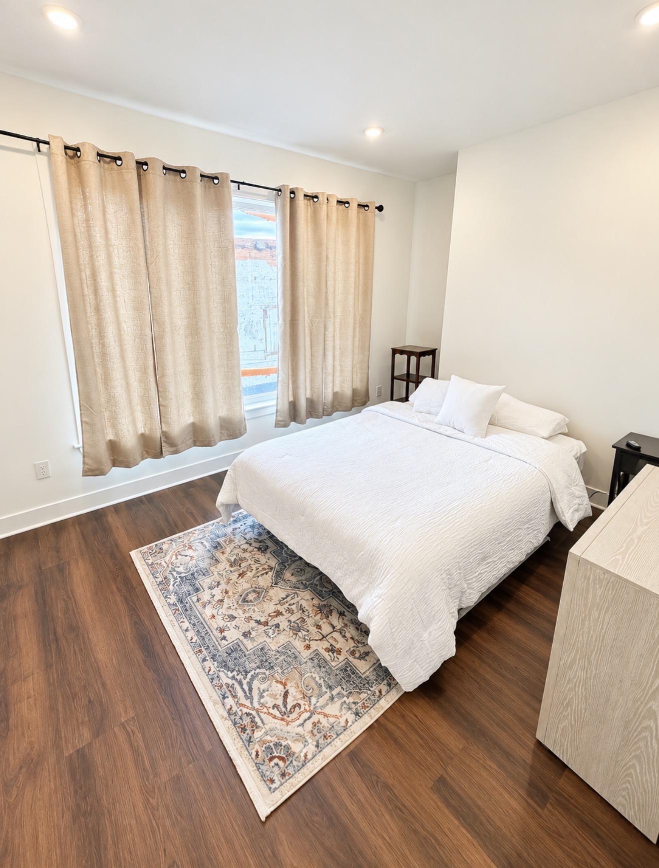 Primary bedroom with white linens, patterned rug and large window