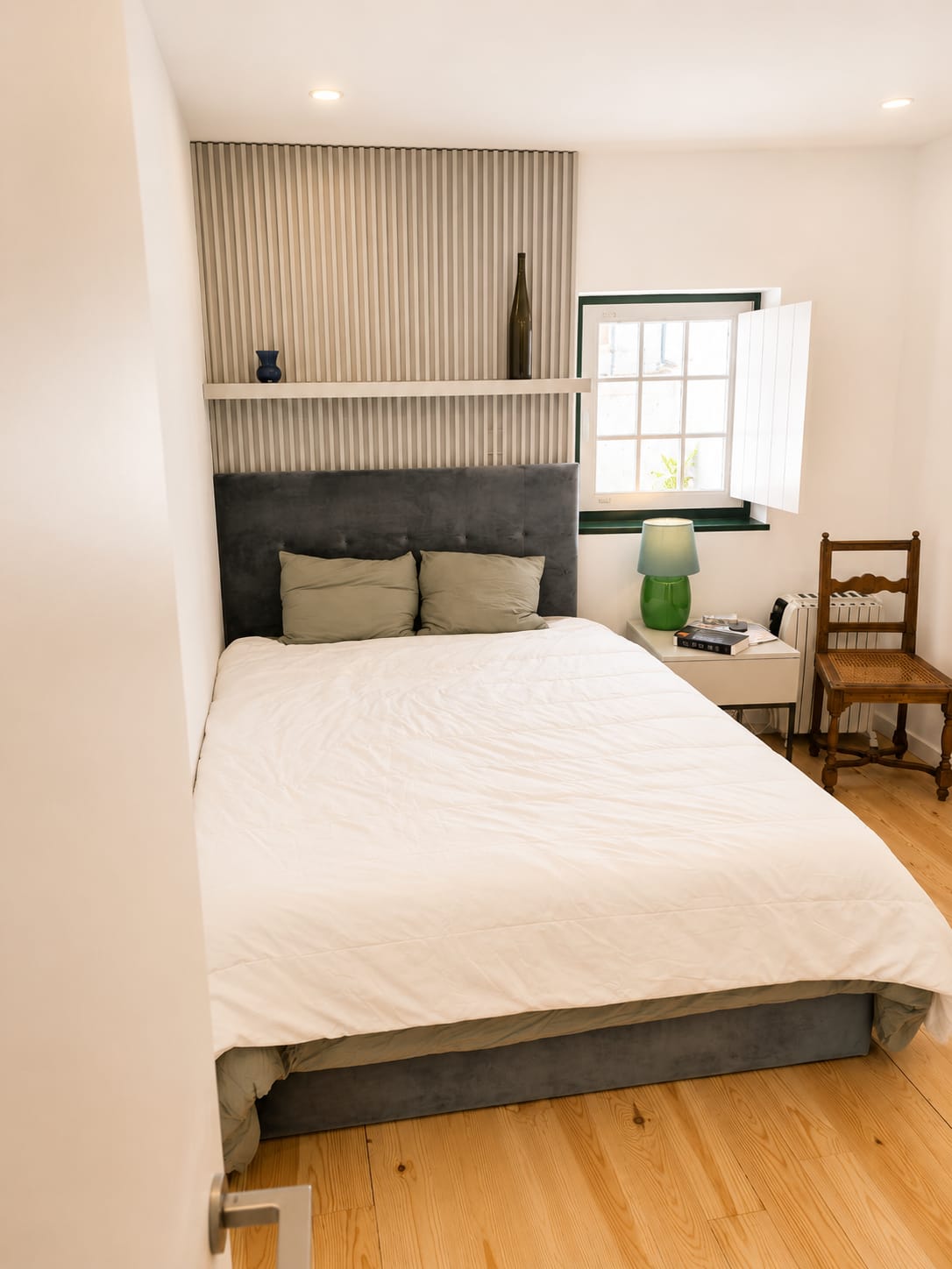 Bedroom with grey velvet headboard, fluted panelling and shuttered window