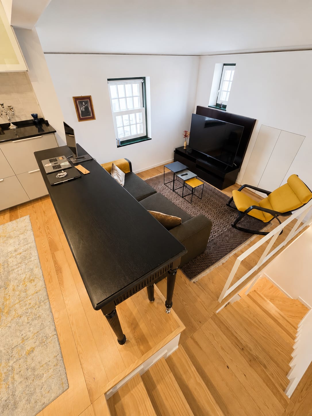 Living area seen from above with sofa, smart TV and mustard rocking chair by tall windows