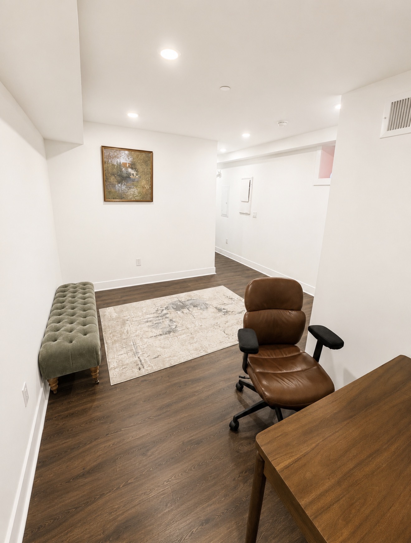 Lower-level office with dark wood desk, leather chair and tufted olive bench