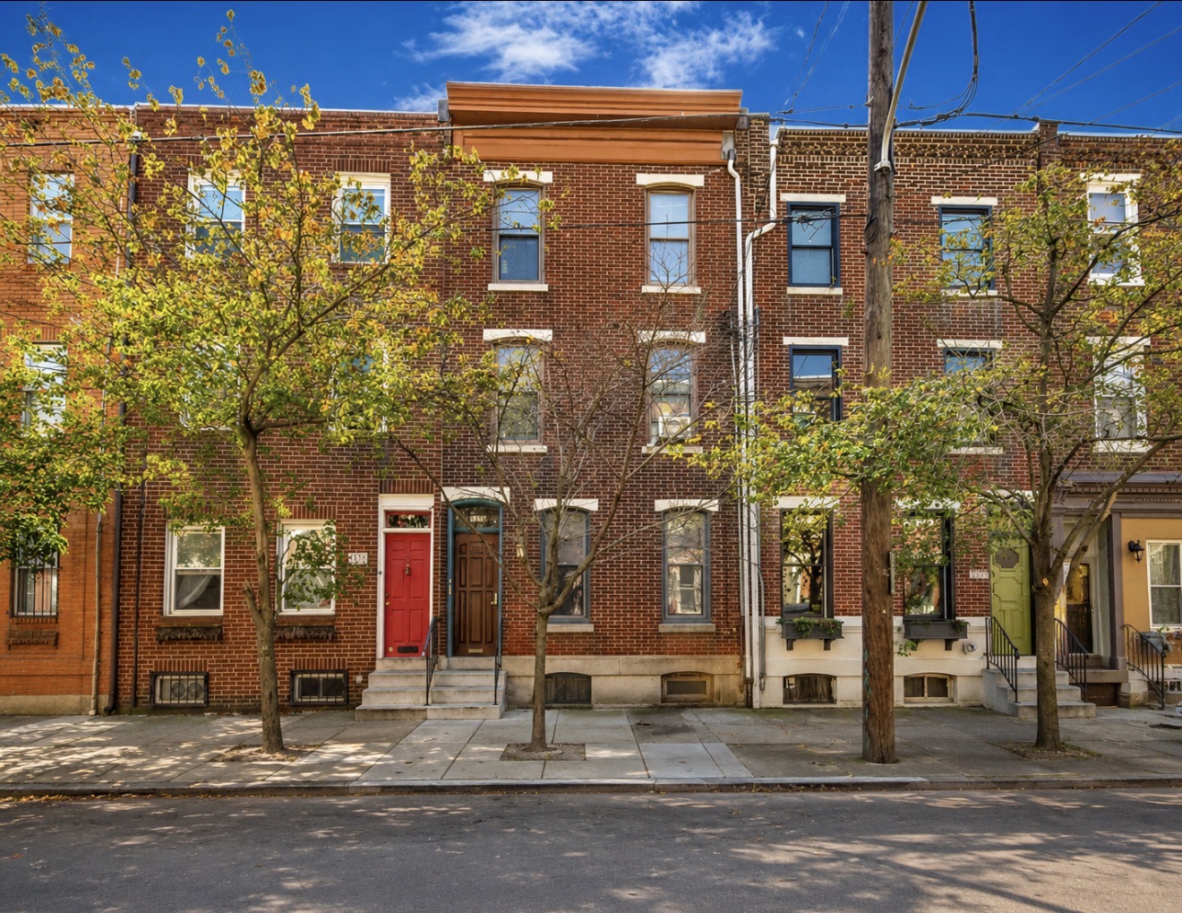 Red brick Philadelphia townhome row with stoops, window boxes and a terra-cotta cornice against a blue sky