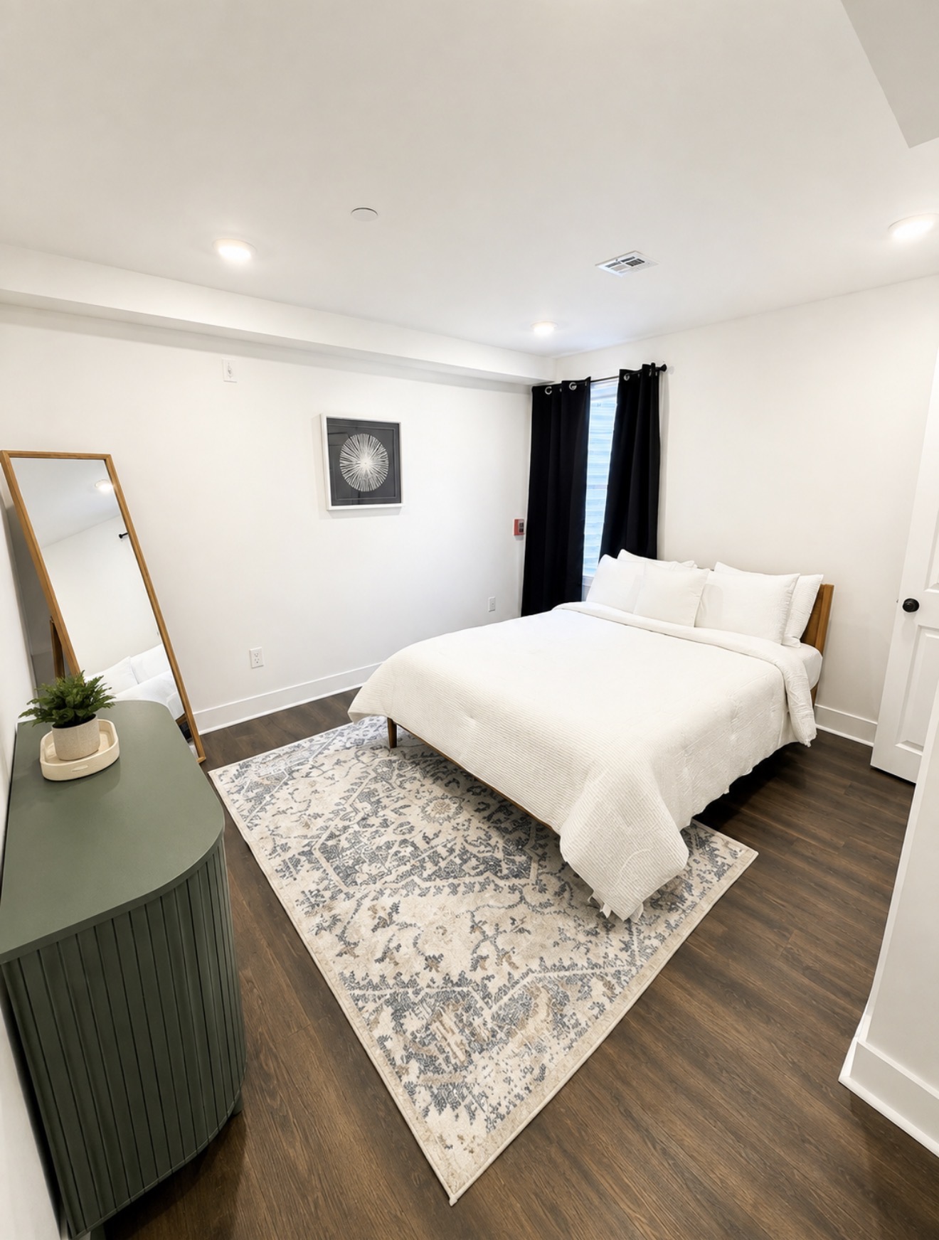 Bedroom with queen bed in white linens, sage green console and full-length mirror