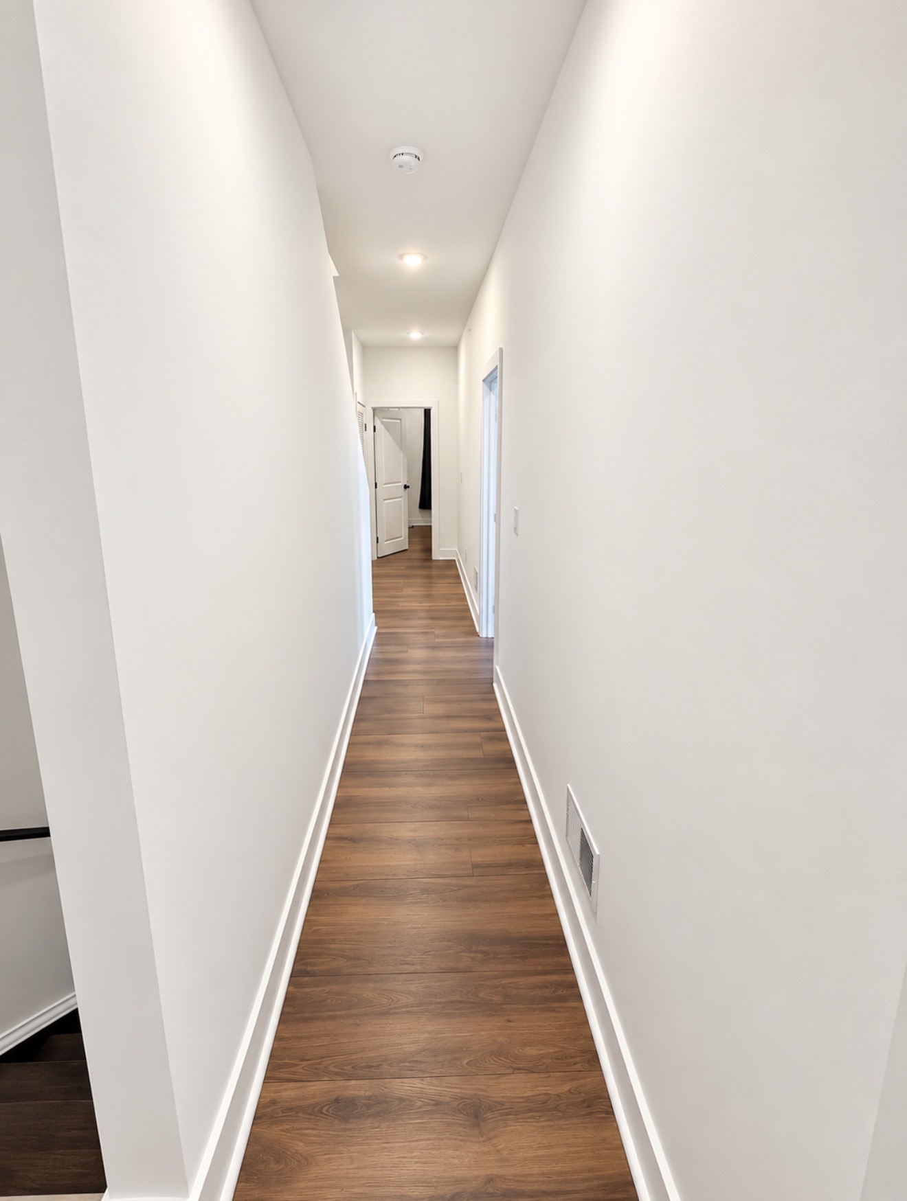 Bright hallway with white doors, recessed lighting and wood-look floors