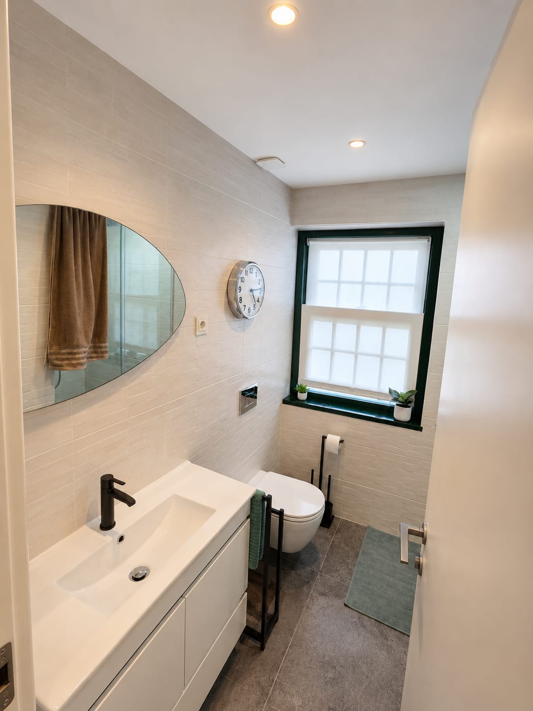 Tiled bathroom with oval mirror, floating white vanity and a shuttered window