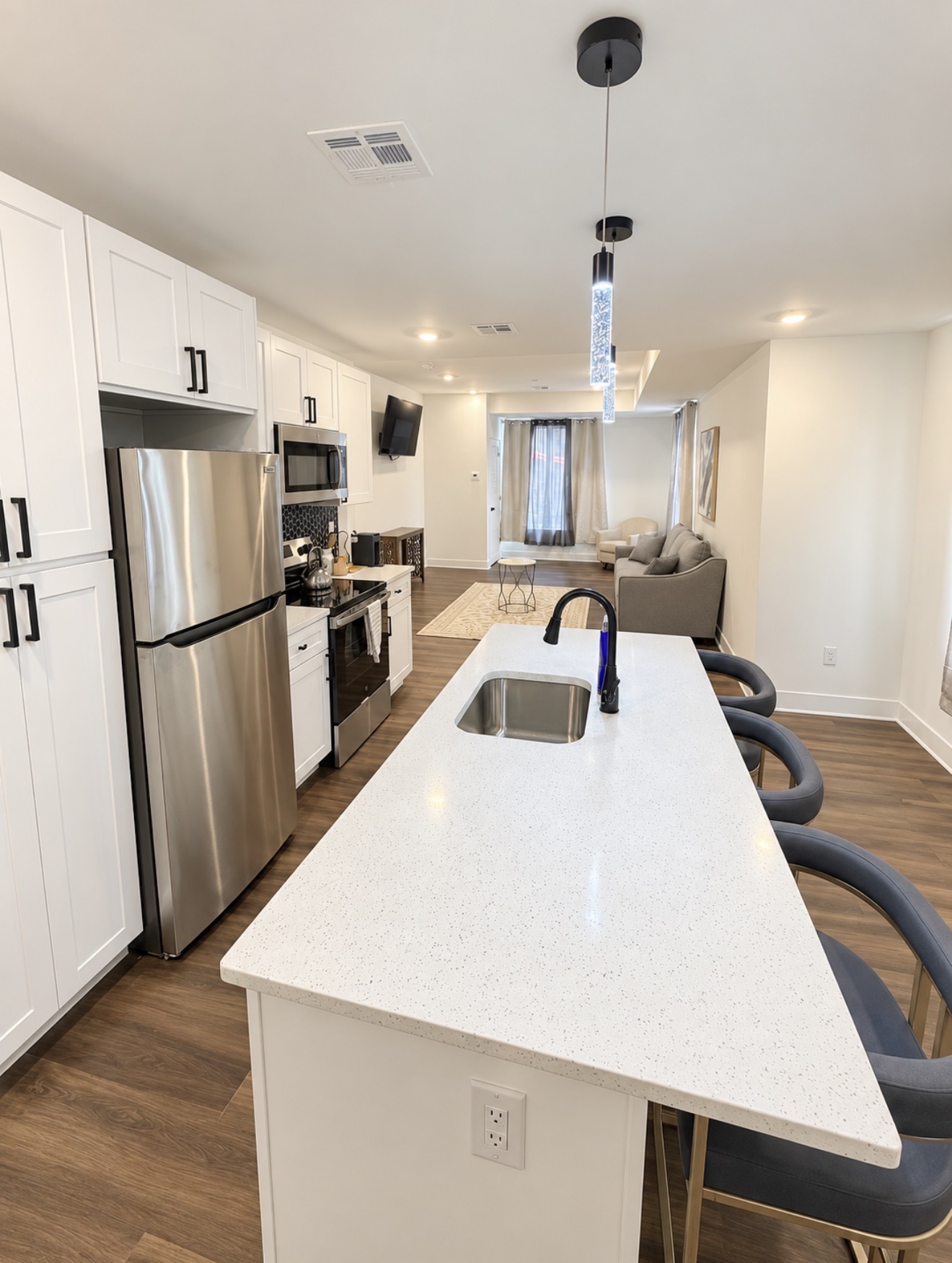 Open kitchen with white island and bar stools looking into a bright living room