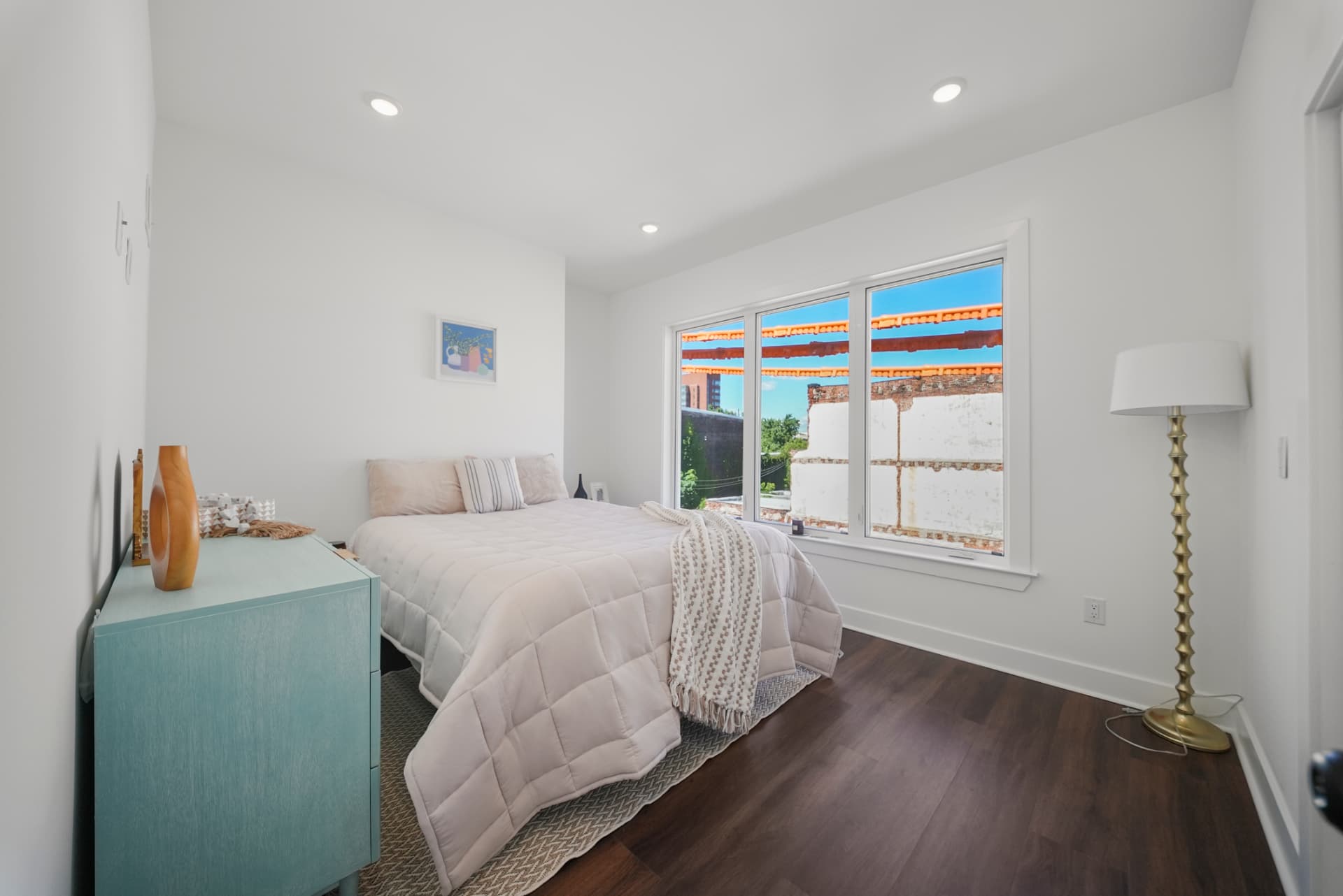 Bedroom with queen bed, teal dresser and large windows overlooking the neighborhood