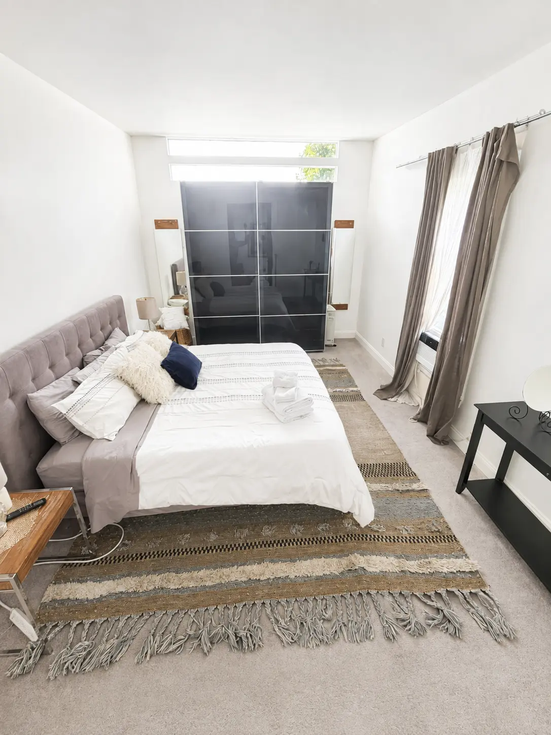 Primary bedroom with upholstered bed, fresh linens and woven area rug
